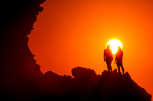 women standing at the edge of a cliff at sunset under a vibrant sky