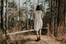 a woman in a dress walking through a forest 