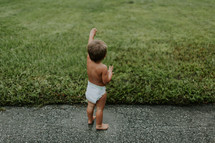 toddler boy in a diaper waving in the grass