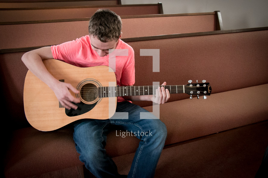 Teen boy playing guitar sitting on a pew
