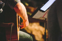 Shot of a man's arm wrapped around a guitar, music stand in front of him