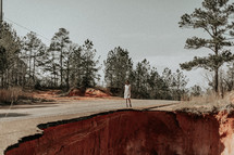 a woman standing at the edge of a collapsed road 