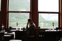 Man in prayer sitting at a table in front of a window in a restaurant.