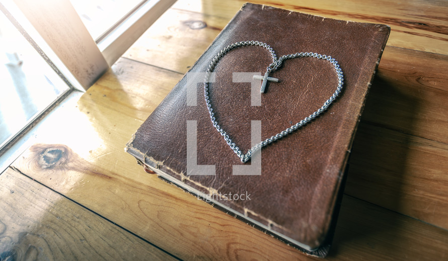 cross necklace in the shape of a heart on a Bible 