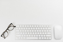 Mouse, keyboard, and glasses on a white desk