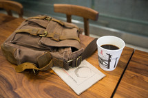 coffee cup and backpack on a wood desk 