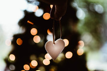 hand holding a heart ornament and bokeh Christmas lights 