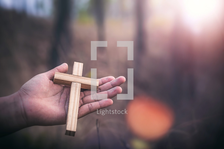 wooden cross in the palm of a hand outdoors 