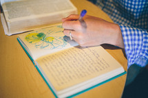 Woman's hand drawing in a notebook with an open bible on the table