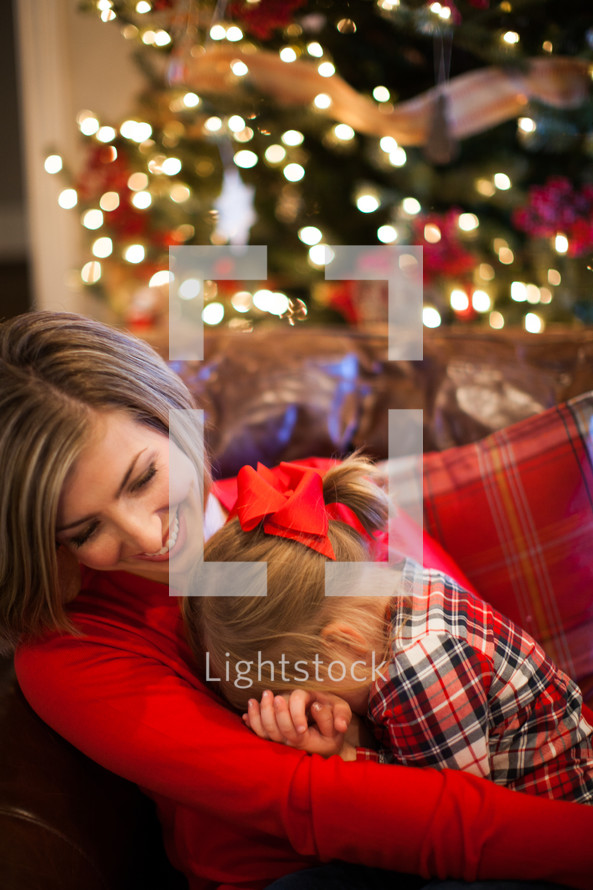 mother and daughter snuggling near a Christmas tree 