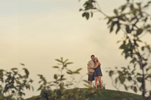 Embracing couple standing on a hilltop.