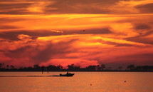 The sky lit by an orange sunset over a boat moving through the water.