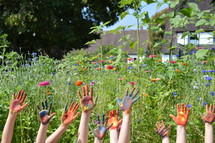finger paint on the hands of kids standing outdoors in a field of flowers 