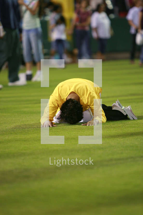 Man prone on face praying bowing before god on grass field crusade salvation. 