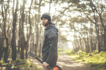 a man holding a guitar in a forest 