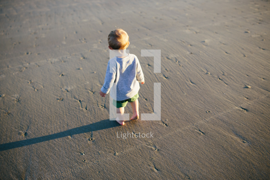 toddler boy standing on sand on a beach 