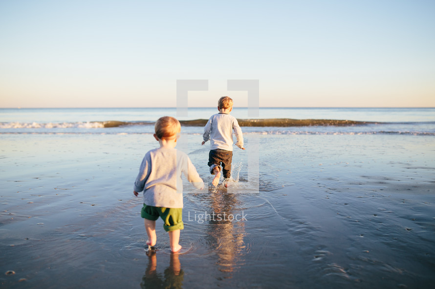 toddler boys running in tide on a beach 