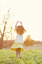 girl child running in a field with her hands in the air