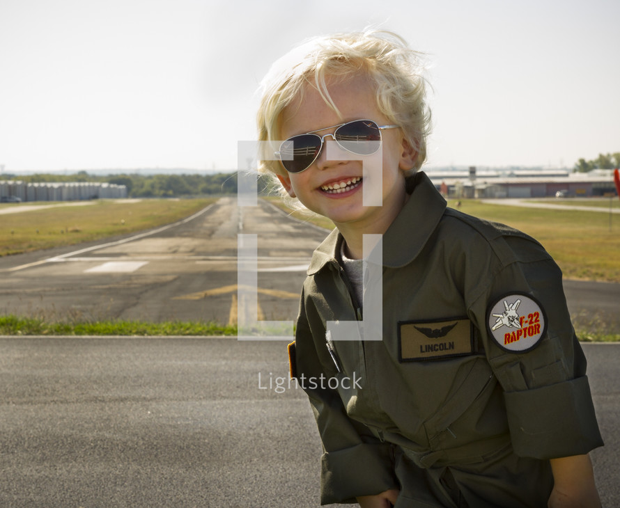 a boy child in a pilot uniform standing in front of a runway 