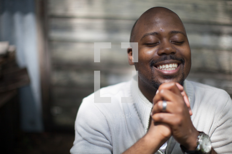 a smiling African American man with praying hands 