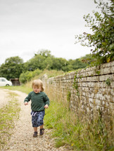 toddler boy running along a gravel path 