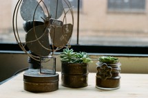 a fan and house plants on a desk 