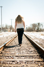teen girl walking on a train tracks 