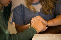 women holding hands in preyer over a Bible 