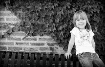 a girl child sitting on a bench and ivy on a wall 