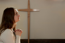 woman with praying hands looking up to God in a church
