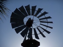 A silhouette image of a large wind mill with its blades reflecting against a night time sky in central Florida. 