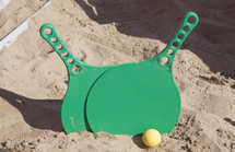 Two green rackets and a ball on the sandy beach.