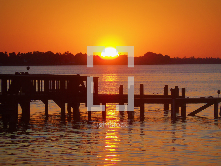 A beautiful orange glow sunset over a pier on a lake signaling the end of another day. 