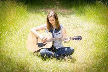 woman sitting in a field playing her guitar