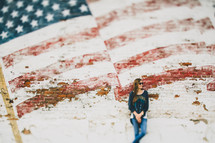 A woman leaning against a wall with a faded flag painted on it.