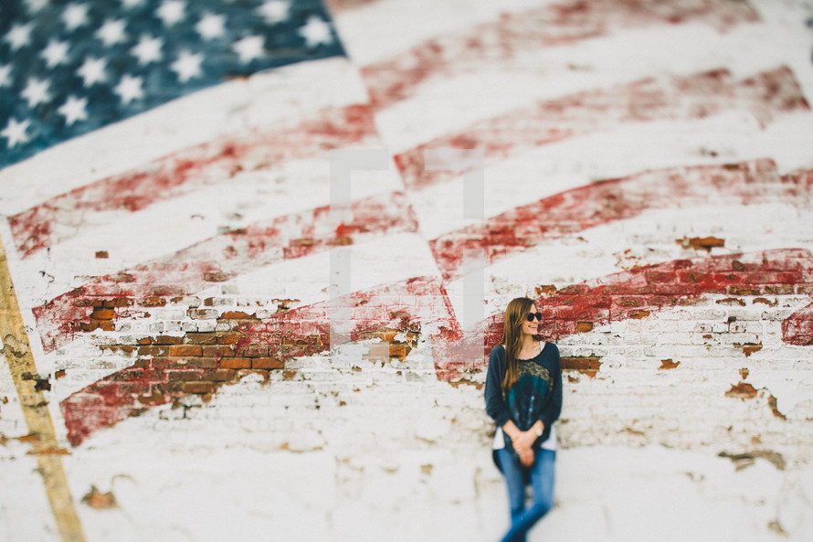 A woman leaning against a wall with a faded flag painted on it.