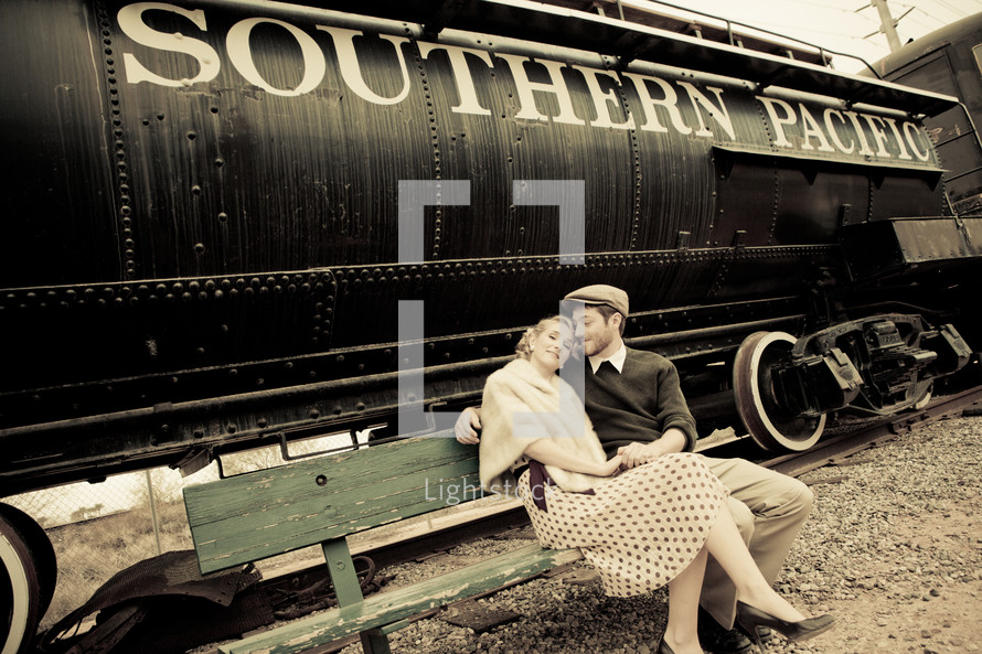Couple sitting on a bench by a train.
