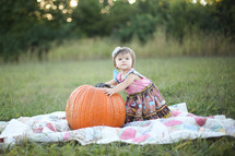 toddler girl on a blanket in the grass with a pumpkin 