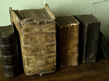 Antique books on a shelf against a stucco wall. 