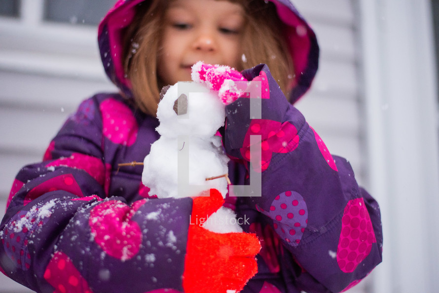 Little girl playing in the snow and making a snowman
