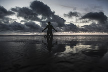a man kneeling on a beach on wet sand at sunset 