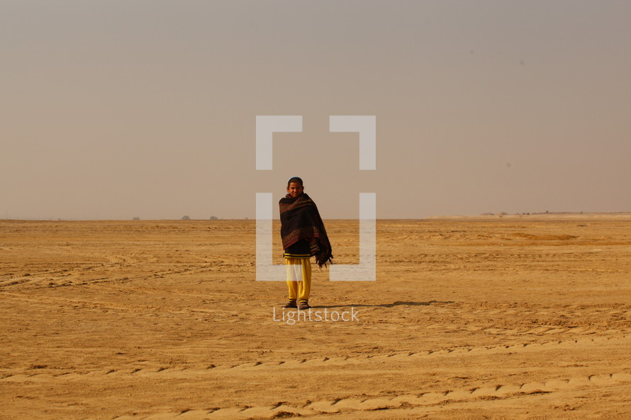 man standing in a desert wrapped in a blanket 