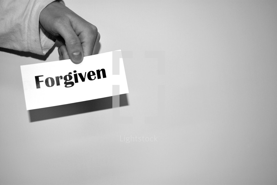 hand holding a piece of paper with the word forgiven 