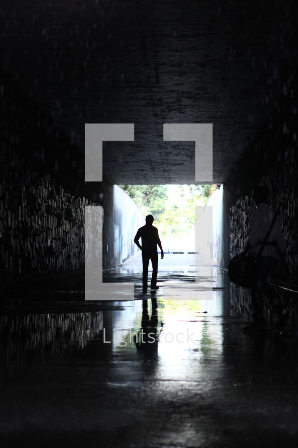 a man walking through a dark wet tunnel 