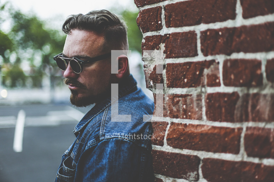 man in sunglasses leaning against a brick wall 