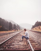 Girl sitting on railroad tracks 