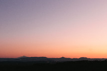 The sun sets on the horizon. A mountain range can be seen in the distance.
