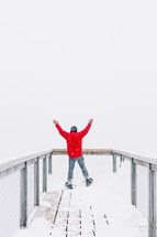 a man standing at the end of an observation deck with hands raised 