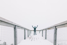a man standing on an observation deck with hands raised in winter 