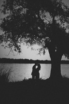 A couple embraces one another at the edge of a pond
